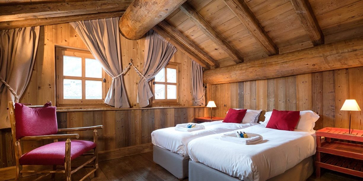 Chalet Farmhouse Val d'Isere Tignes-Val d'Isere Frankrijk wintersport skivakantie luxe slaapkamer aparte bedden rode kussens rode stoel ramen nachtkastje
