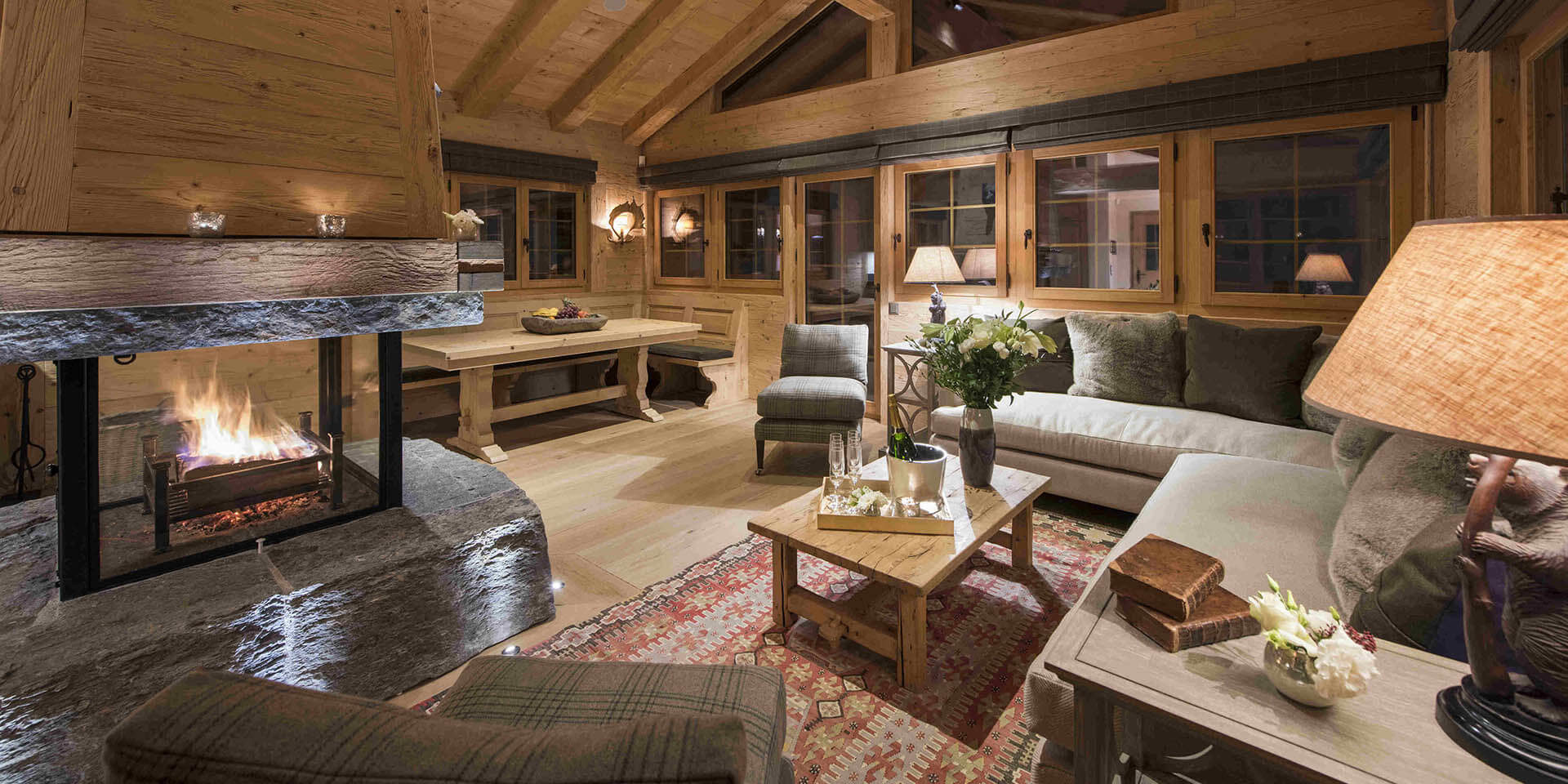 Chalet Chouqui Verbier Les 4 Vallees Zwitserland wintersport skivakantie luxe living open haard hoekbank kussens fauteuils salontafel Champagne eethoek eettafel bankje lampen ramen houten balken