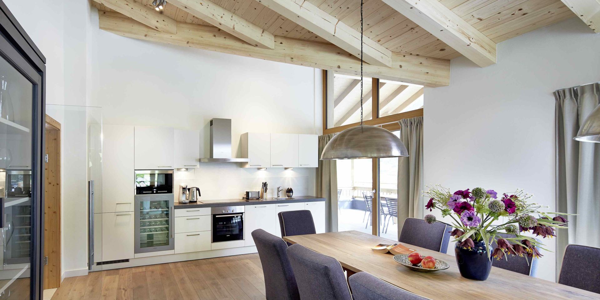 Kaprun Glacier Estate Zell am See-Kaprun Oostenrijk wintersport skivakantie luxe Penthouse K10 eettafel stoelen bloemen lampen keuken houten balken balkon stoelen