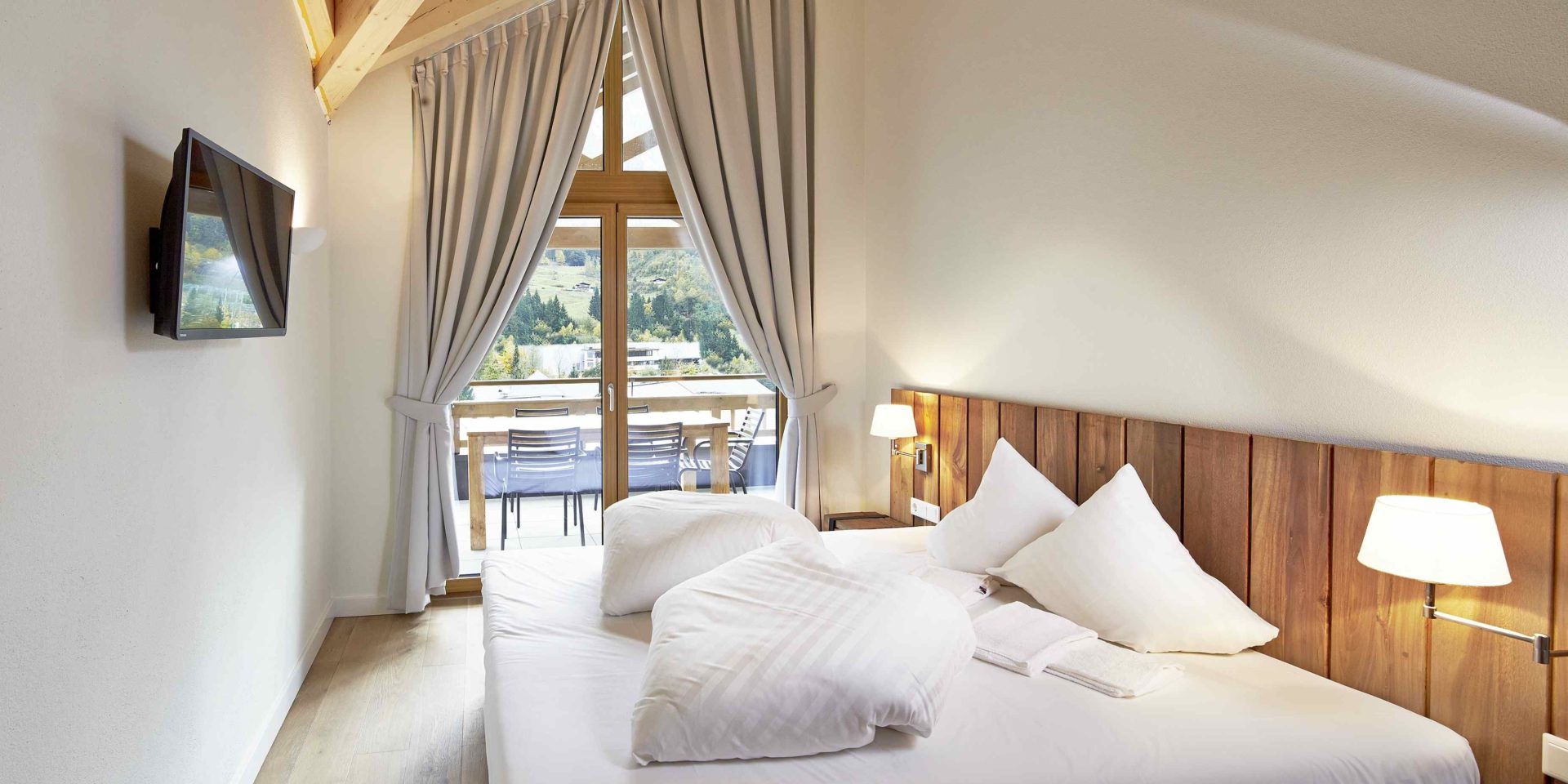 Kaprun Glacier Estate Zell am See-Kaprun Oostenrijk wintersport skivakantie luxe slaapkamer K8 2-persoonsbed nachtlampjes TV balkon stoelen hoge ramen gordijnen