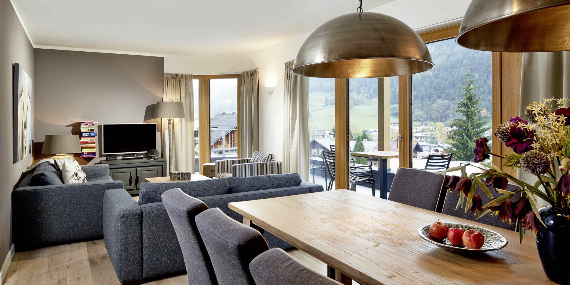 Kaprun Glacier Estate Zell am See-Kaprun Oostenrijk wintersport skivakantie luxe woonkamer K6 eettafel stoelen bloemen lampen banken fauteuil TV kast schilderij grote ramen balkon zitje stoelen tafel