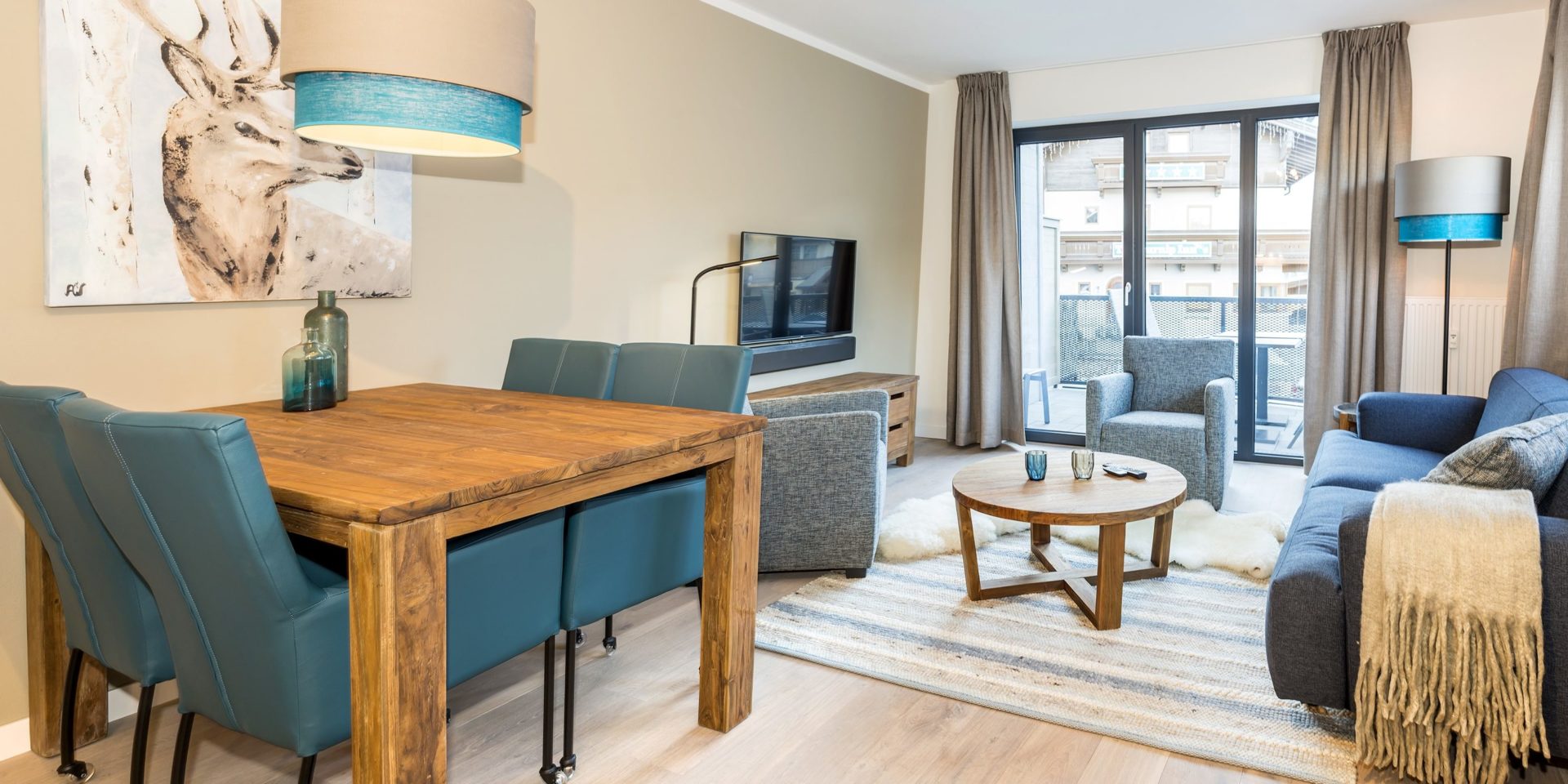 Kristall Plaza Niederau Wildschonau Oostenrijk wintersport skivakantie luxe appartement P4C blauwe bank fauteuils salontafel TV hoge ramen eettafel stoelen lamp schilderij hert