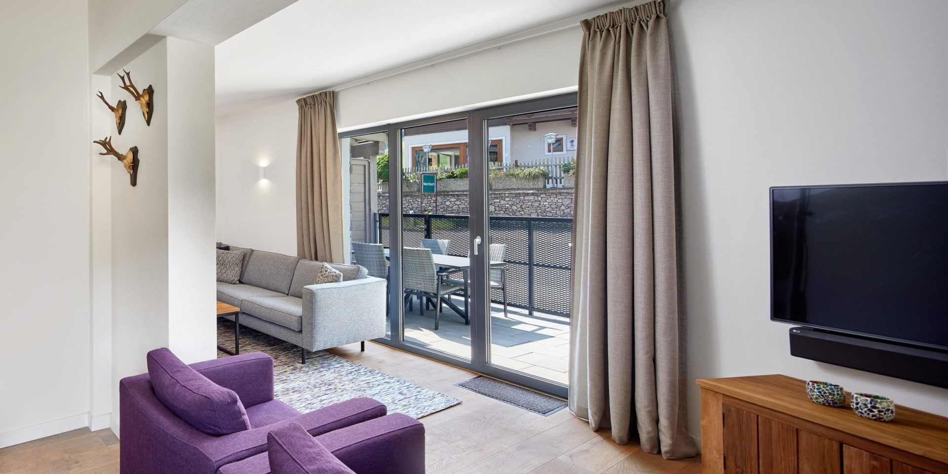 Kristall Plaza Niederau Wildschonau Oostenrijk wintersport skivakantie luxe appartement P6A bank paarse fauteuils TV hoge ramen gewei balkon tafel stoelen
