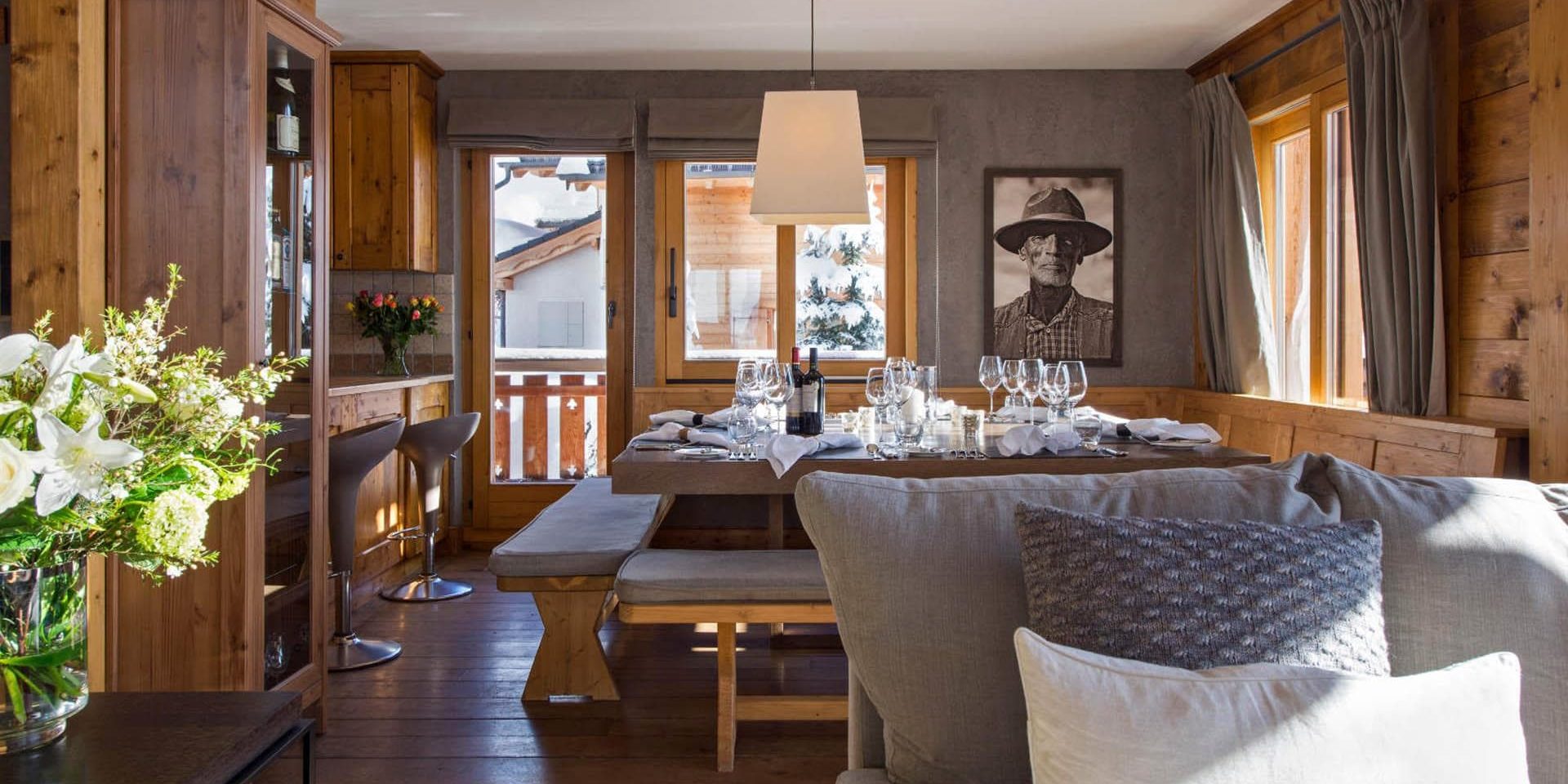 Chalet Pierre Avoi Verbier Les 4 Vallees Zwitserland wintersport skivakantie luxe eetkamer gedekte tafel wijn wijnglazen schilderij bloemen bank barkrukken lamp balkon kussens