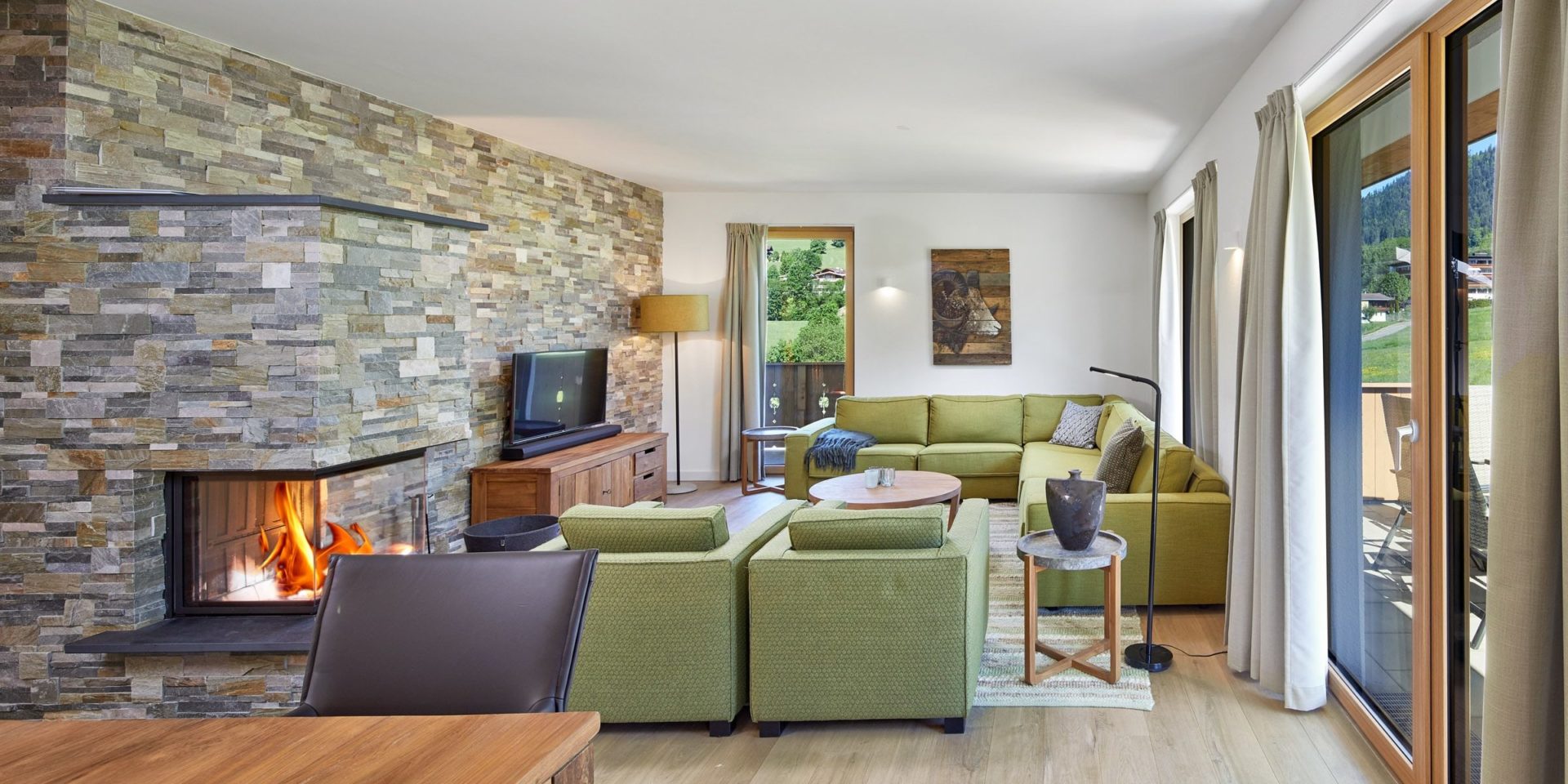 Residenz Drachenstein Niederau Wildschonau Oostenrijk wintersport skivakantie luxe appartement D7 groene banken fauteuils salontafel TV eettafel stoel open haard vloerkleed balkon zitje hoge ramen