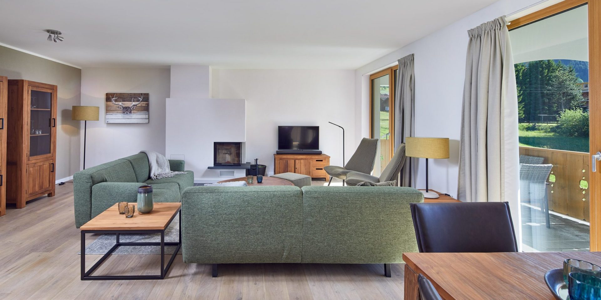 Residenz Drachenstein Niederau Wildschonau Oostenrijk wintersport skivakantie luxe appartement D8 groene banken fauteuils salontafel TV eettafel stoel open haard vloerkleed kast balkon zitje hoge ramen bomen