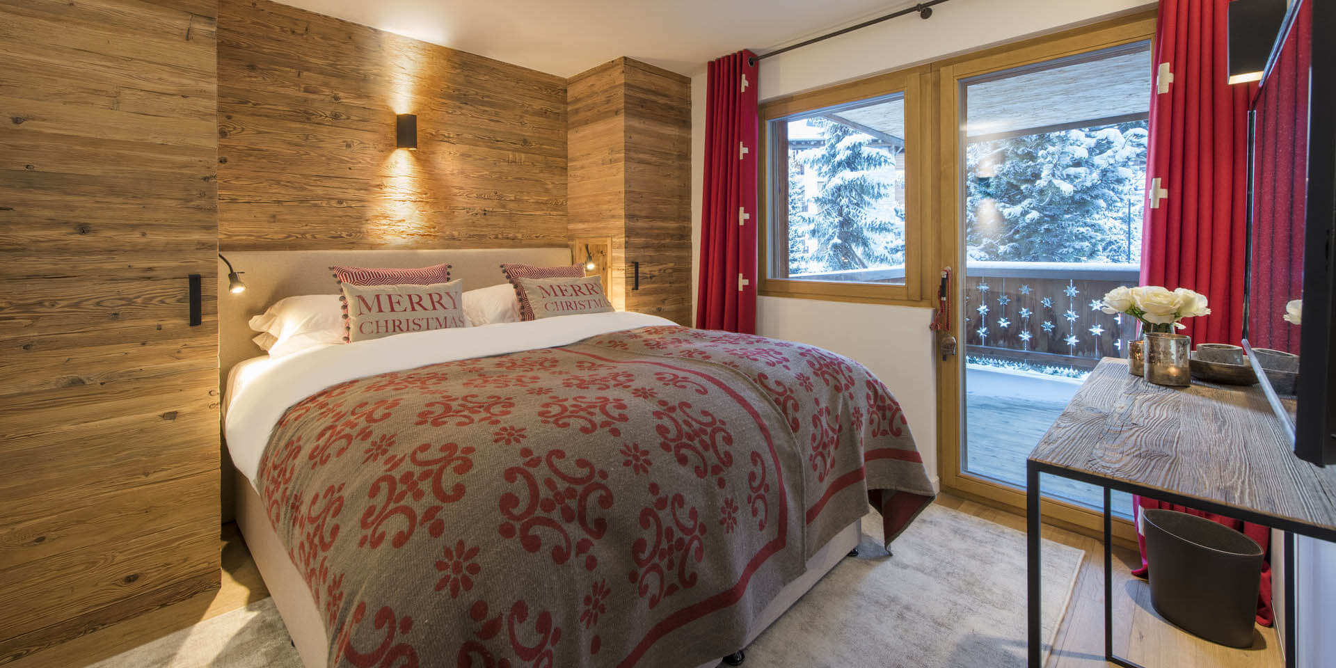 Appartement Rosalp 4 Verbier Les 4 Vallees Zwitserland wintersport skivakantie luxe slaapkamer 2-persoonsbed sprei kussens Merry Christmas tafel rode gordijnen balkon besneeuwde bomen