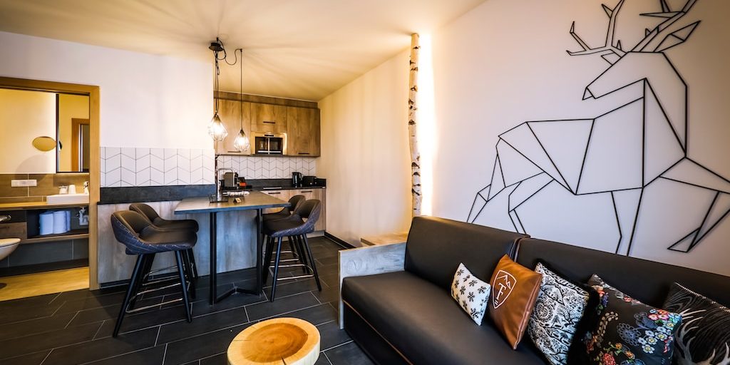 Hotel 24 by Avenida Kaprun Zell am See-Kaprun Oostenrijk wintersport skivakantie luxe 1 slaapkamer suite 2 personen leren bank kussens krukje hert boomstam keuken bar barkrukken hanglampen badkamer wastafel spiegel