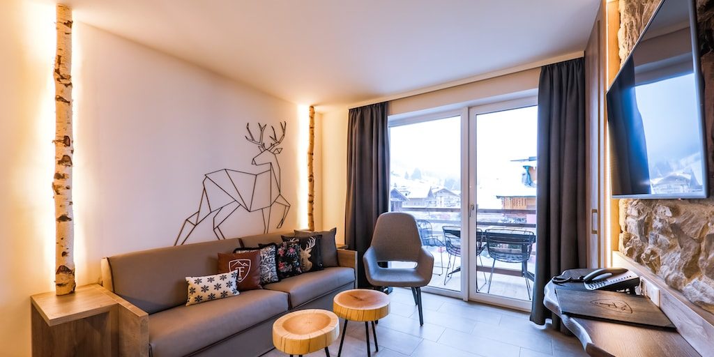 Hotel 24 by Avenida Kaprun Zell am See-Kaprun Oostenrijk wintersport skivakantie luxe 2 slaapkamer suite living bank kussens fauteuil krukjes TV hert boomstam balkon zitje tafel stoelen