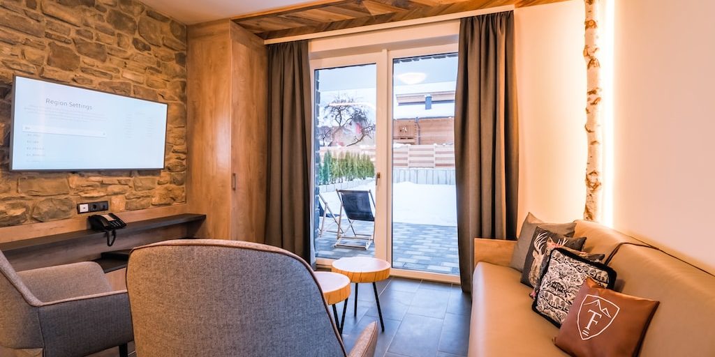Hotel 24 by Avenida Kaprun Zell am See-Kaprun Oostenrijk wintersport skivakantie luxe 3-slaapkamer suite living bank kussens fauteuils TV stenen muur boomstam krukjes terras ligstoelen