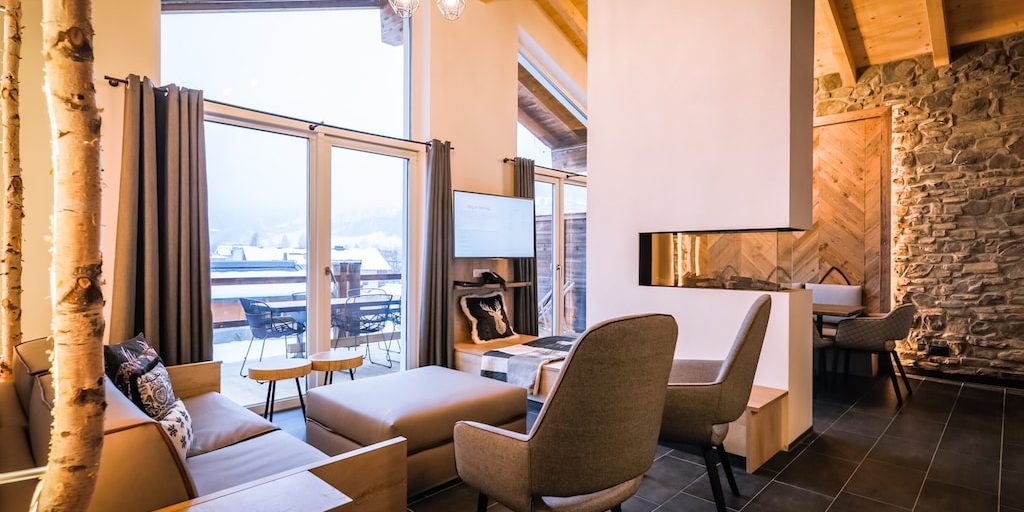 Hotel 24 by Avenida Kaprun Zell am See-Kaprun Oostenrijk wintersport skivakantie luxe Penthouse 3 slaapkamers living open haard bank fauteuils hocker krukjes TV eetkamer eettafel stoelen balkon zitje tafel stoelen grote ramen houten balken