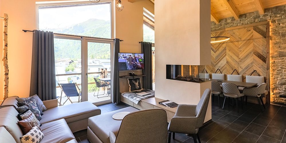 Hotel 24 by Avenida Kaprun Zell am See-Kaprun Oostenrijk wintersport skivakantie luxe Penthouse 4 slaapkamers living open haard bank chaise longue kussens fauteuils TV eetkamer balkon tafel stoelen houten balken grote ramen
