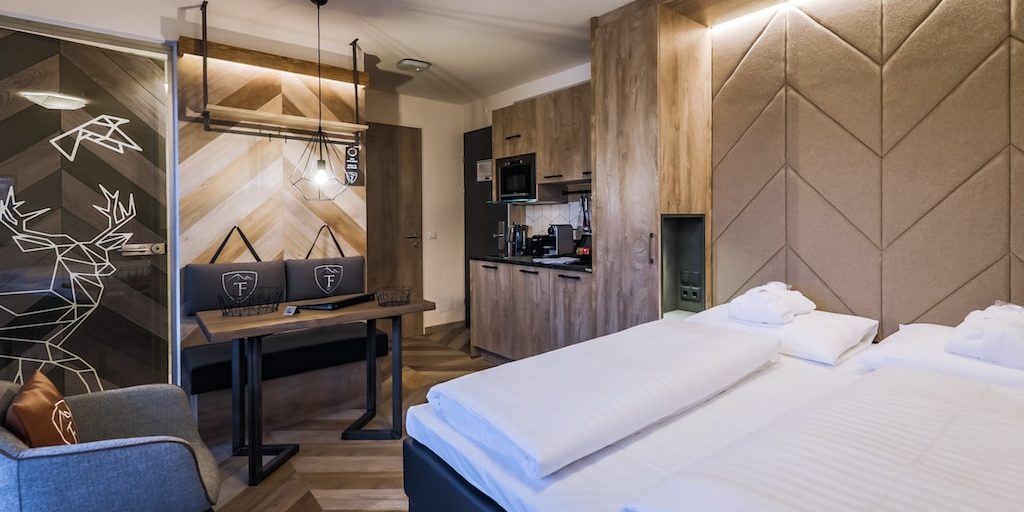 Hotel 24 by Avenida Kaprun Zell am See-Kaprun Oostenrijk wintersport skivakantie luxe Studio 2-persoonsbed fauteuil bankje tafel hanglamp keukenblok hout kastenwand hert vogel