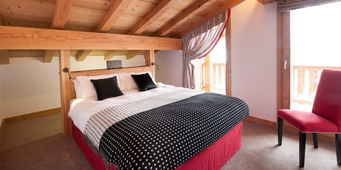 Altitude Lodge Les Gets les Portes du Soleil Frankrijk wintersport skivakantie luxe slaapkamer 2-persoonsbed zwarte kussens rode stoel houten balken houten plafond balkon