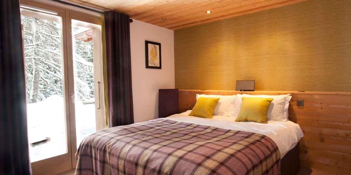 Altitude Lodge Les Gets les Portes du Soleil Frankrijk wintersport skivakantie luxe slaapkamer 2-persoonsbed gele kussens geblokte sprei groene muur schilderij raam besneeuwde bomen
