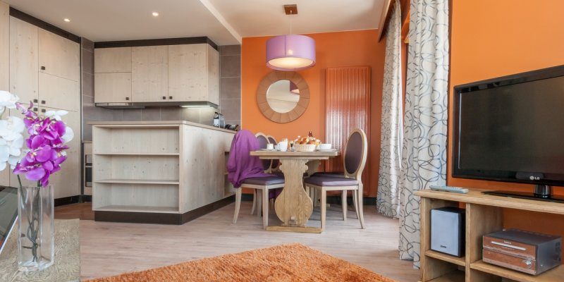 Residence l'Amara Avoriaz Les Portes du Soleil Frankrijk wintersport skivakantie luxe gedekte tafel ontbijt vers fruit stoelen keuken hanglamp spiegel TV Orchidee vloerkleed oranje muur