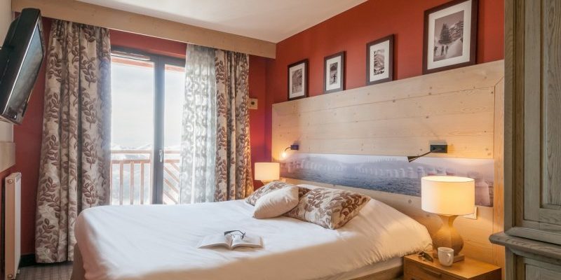 Residence l'Amara Avoriaz Les Portes du Soleil Frankrijk wintersport skivakantie luxe slaapkamer 2-persoonsbed houten hoofdbord schilderijen nachtlampjes TV raam balkon rode muur