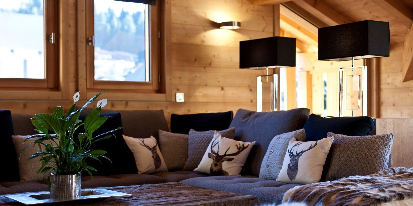Appartement No. 5 Les Gets Les Portes du Soleil Frankrijk wintersport skivakantie luxe living lounge bank kussens herten salontafel plant lampen houten wand ramen bomen sneeuw