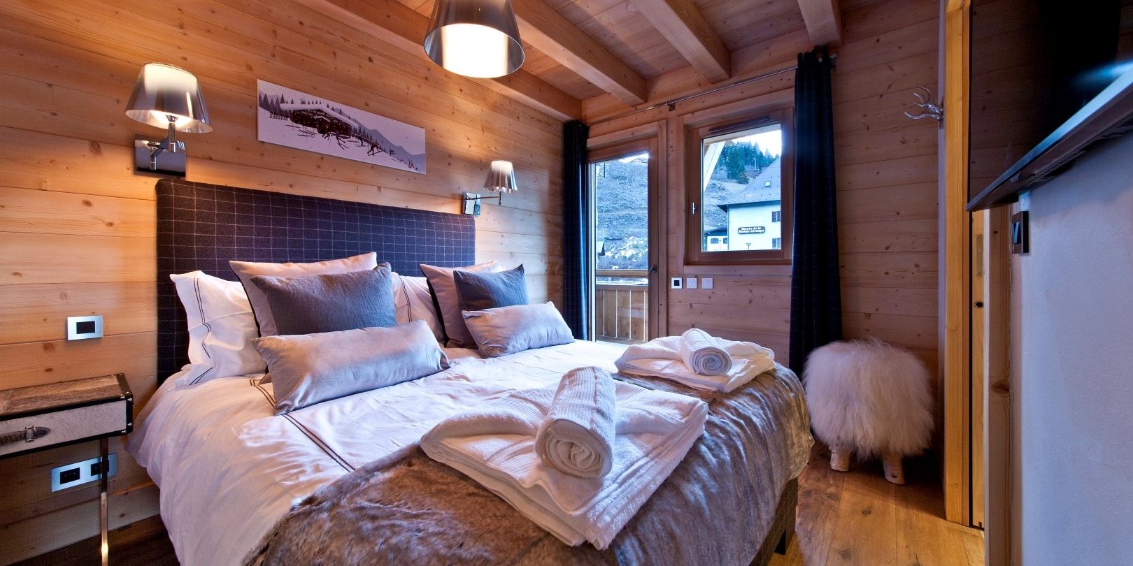Appartement No. 5 Les Gets Les Portes du Soleil Frankrijk wintersport skivakantie luxe slaapkamer 2-persoonsbed kussens handdoeken hocker schilderij TV raam balkon houten balken houten wanden bomen
