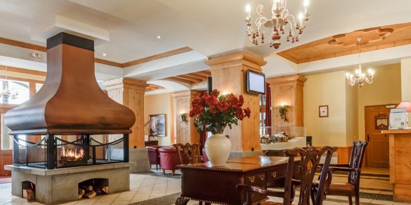 Arc 1950 le Village Arc 1950 Paradiski Frankrijk wintersport skivakantie luxe receptie Prince des Cimes open haard houten tafel houten stoelen bloemen rode fauteuils kroonluchter hout