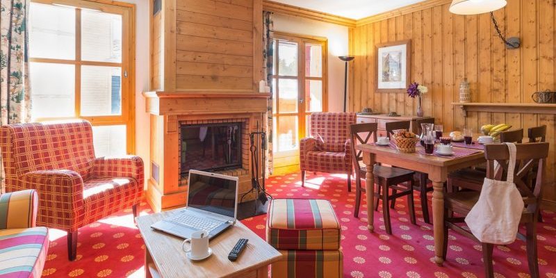 Arc 1950 le Village Arc 1950 Paradiski Frankrijk wintersport skivakantie luxe living open haard gekleurde bank hocker rode fauteuils gedekte tafel houten stoelen ramen houten wand hanglamp