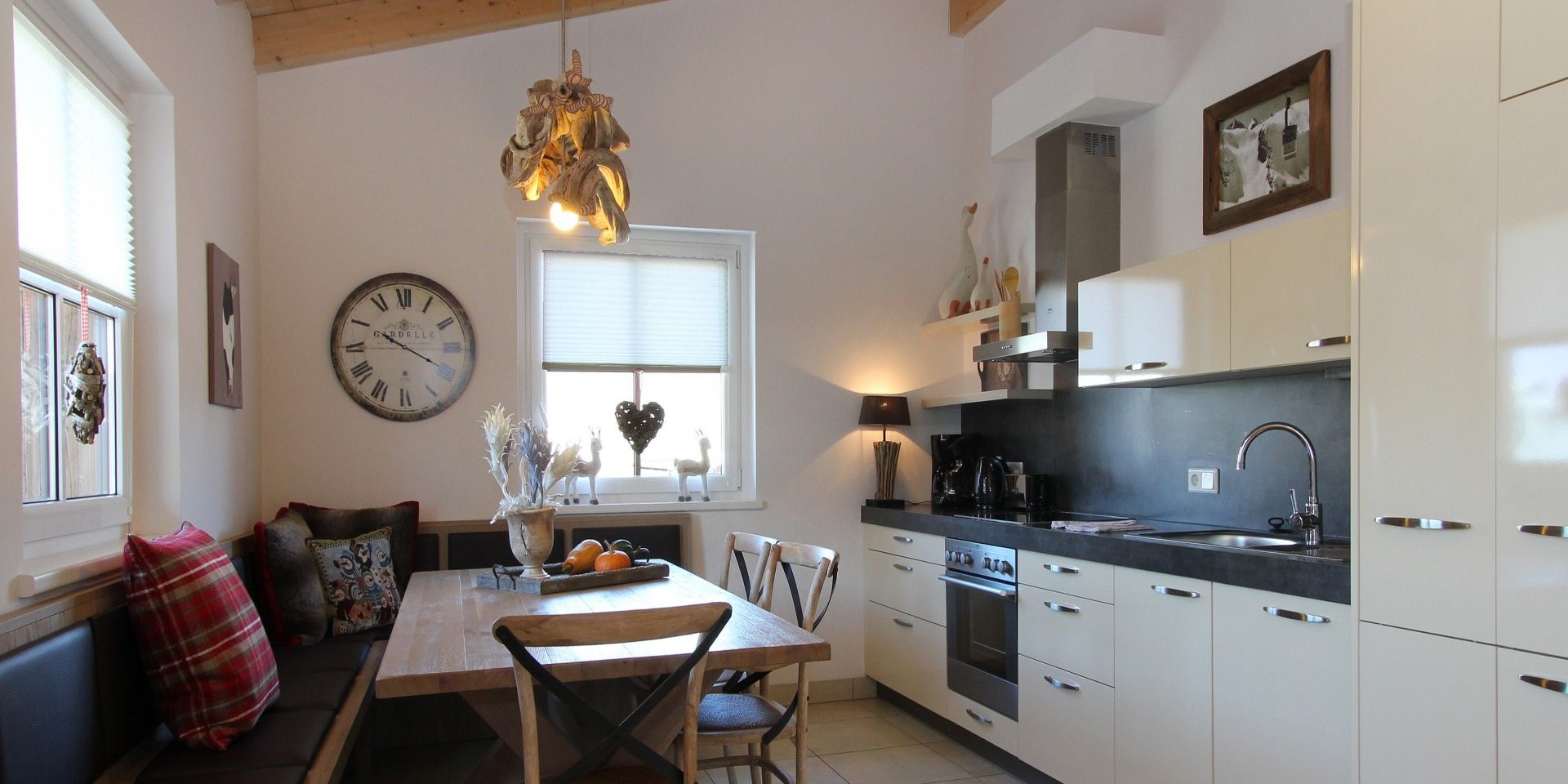 Avenida Mountain Resort Kaprun Zell am See-Kaprun Oostenrijk wintersport skivakantie luxe A23 eettafel houten stoelen hoekbank geruit kussen hanglamp keuken afzuigkap schilderij raam klok