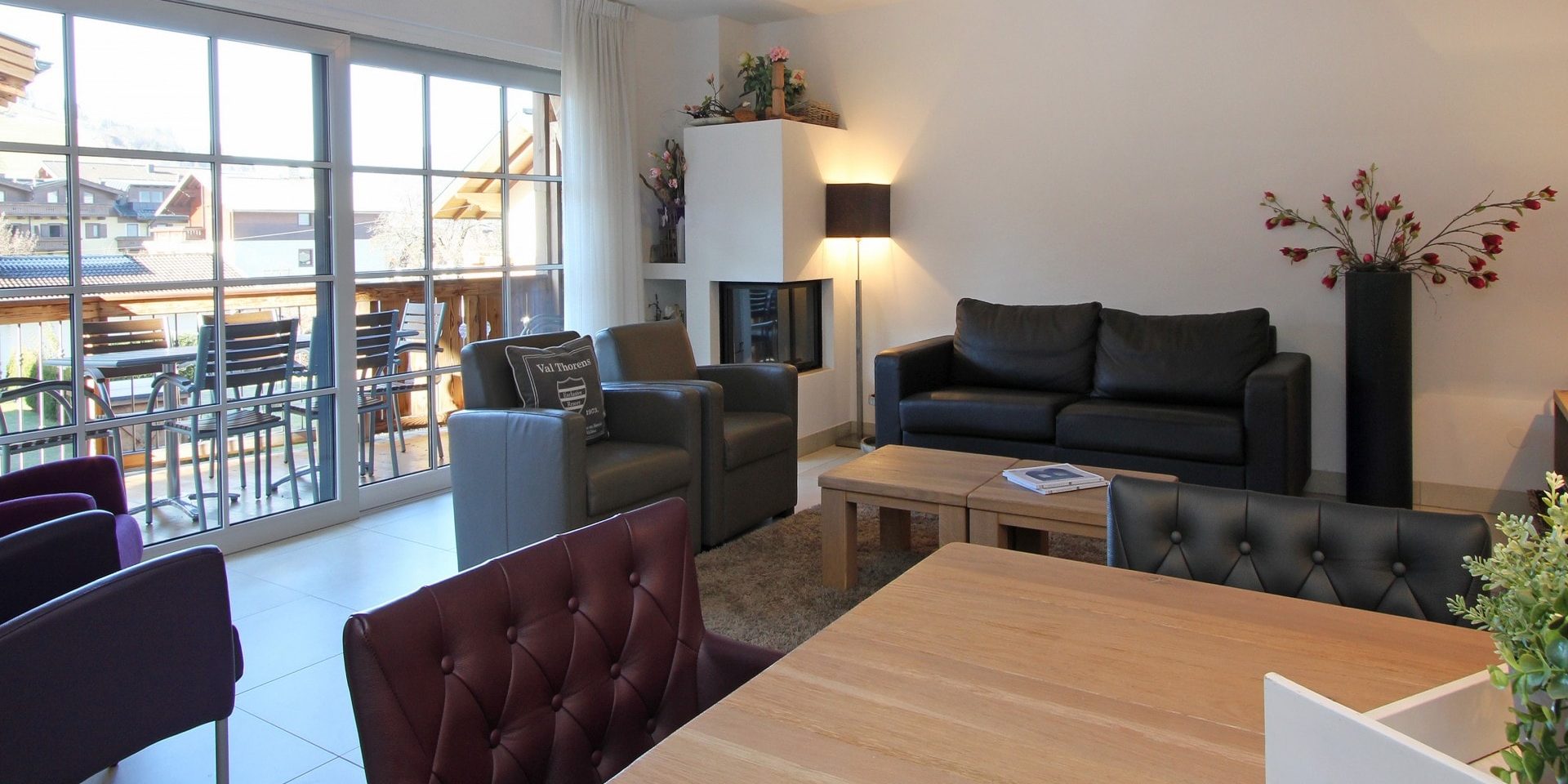 Avenida Mountain Resort Kaprun Zell am See-Kaprun Oostenrijk wintersport skivakantie luxe A12 living zwarte bank grijze fauteuils salontafels planten eettafel leren stoelen paarse fauteuils balkon tafel stoelen open haard