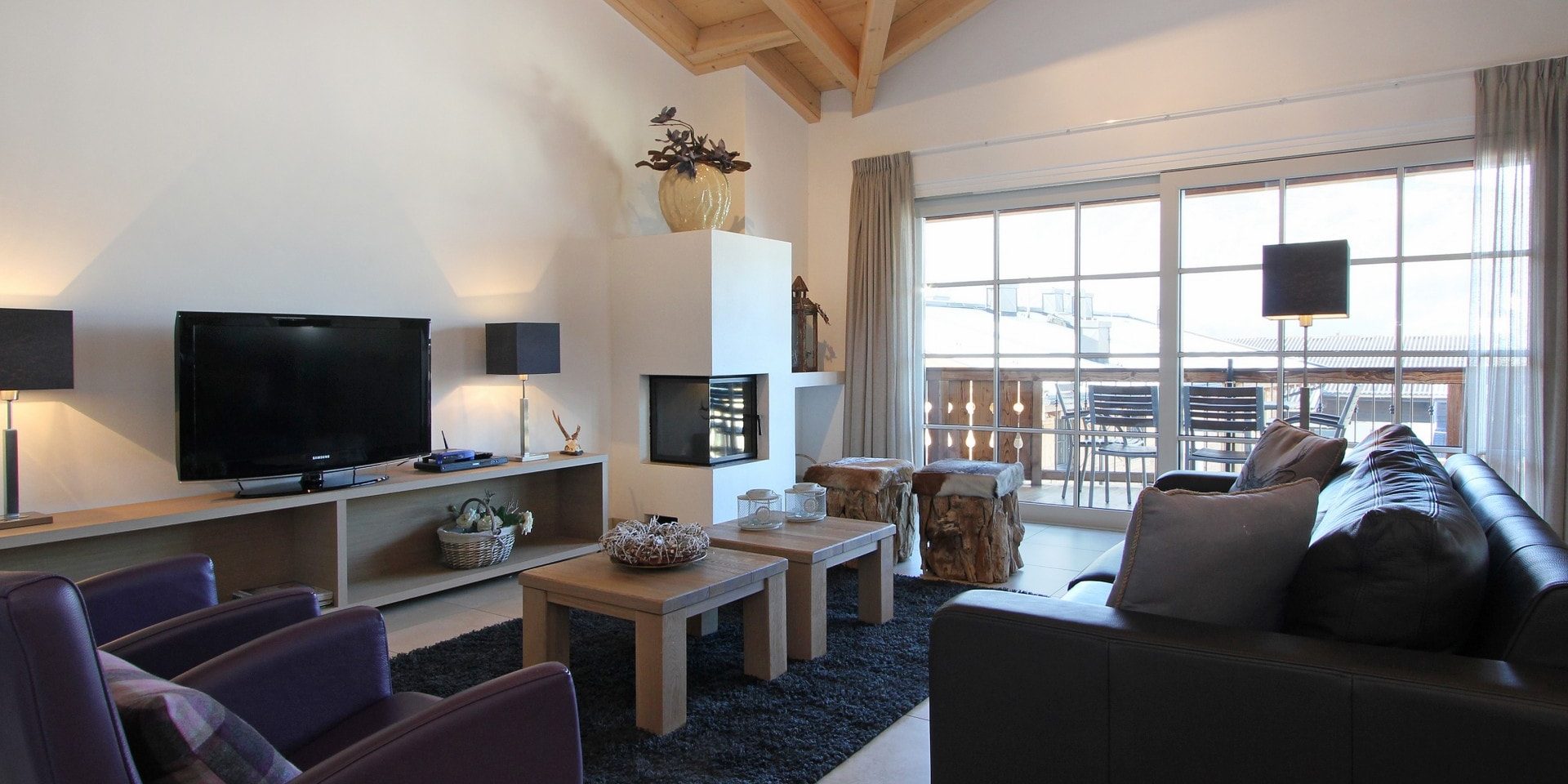 Avenida Mountain Resort Kaprun Zell am See-Kaprun Oostenrijk wintersport skivakantie luxe A23 living zwarte bank grijze fauteuils salontafels planten eettafel leren stoelen paarse fauteuils balkon tafel stoelen open haard