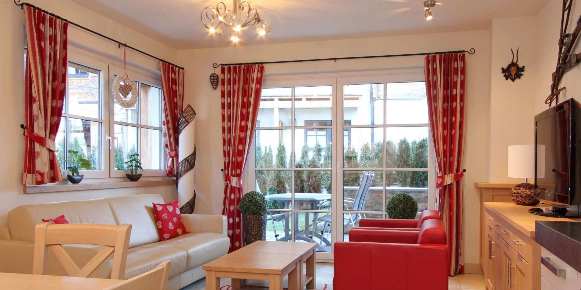Avenida Mountain Resort Kaprun Zell am See-Kaprun Oostenrijk wintersport skivakantie luxe E10 witte bank rode kussens rode fauteuils salontafels kroonluchter ski's TV kast grote ramen terras tafel stoelen rode gordijnen witte hartjes