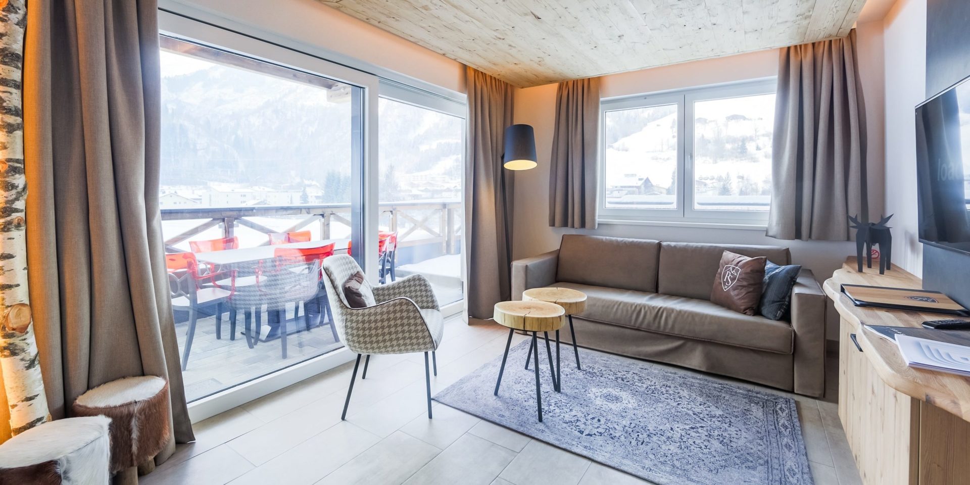 Hotel Avenida Panorama Suites Kaprun Zell am See-Kaprun Oostenrijk wintersport skivakantie luxe Suites 311 312 living bank fauteuil krukjes hockers TV ramen balkon tafel rode stoelen bomen bergen sneeuw