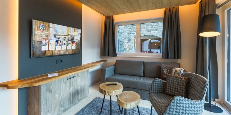 Hotel Avenida Panorama Suites Kaprun Zell am See-Kaprun Oostenrijk wintersport skivakantie luxe Suites 113 114 living bank fauteuil krukjes TV kast vloerkleed raam gordijnen