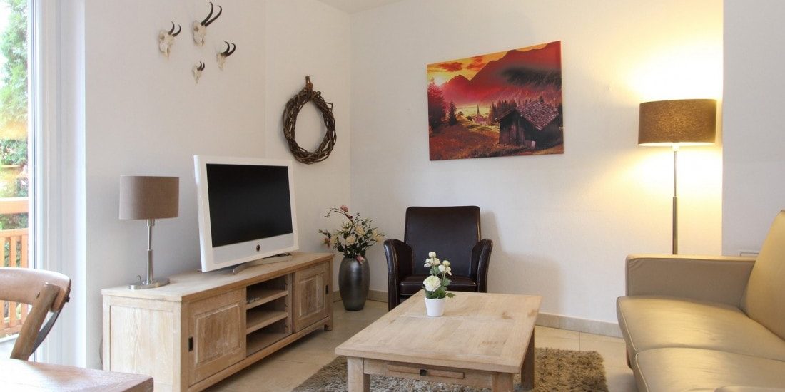 Avenida Style Kaprun Zell am See-Kaprun Oostenrijk wintersport skivakantie luxe Top 1 living bank zwarte fauteuil TV salontafel schilderij gewei plant raam vloerkleed tafel stoel