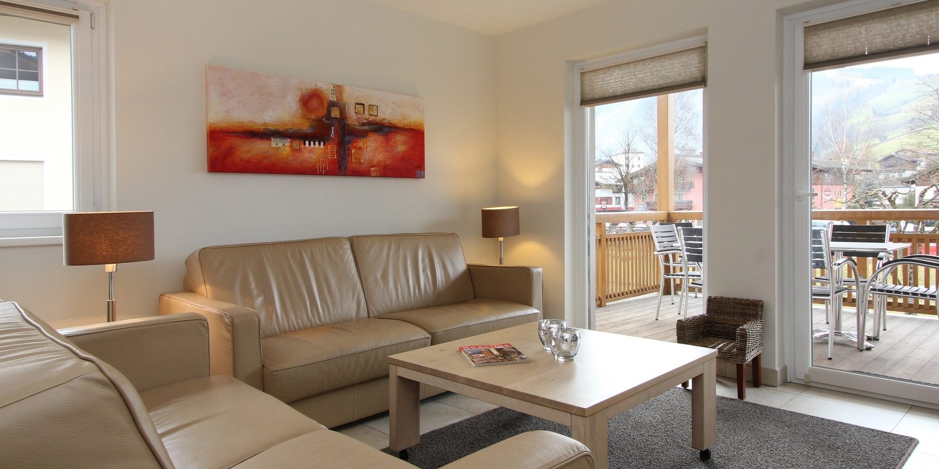 Avenida Style Kaprun Zell am See-Kaprun Oostenrijk wintersport skivakantie luxe Top 5 living witte leren banken salontafel schilderij kaarsen kinderstoeltje lampen balkon tafel stoelen dorp bomen