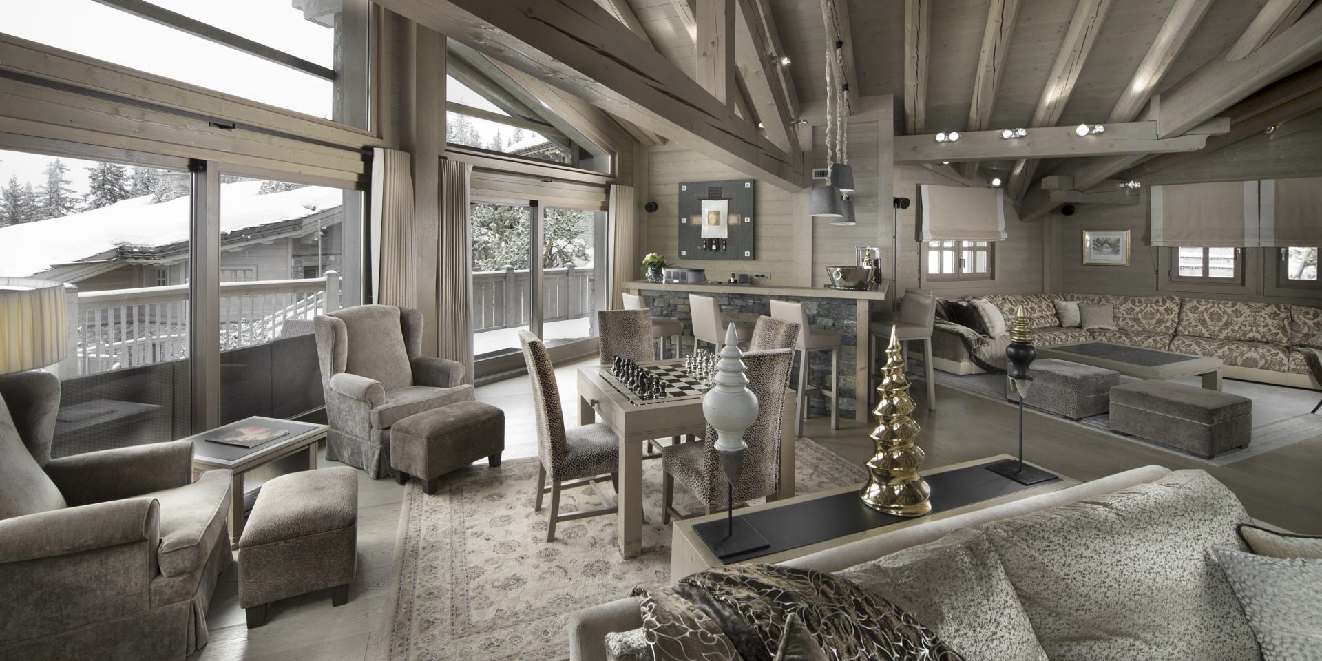 Le K2 Palace Suite-Chalet Abruzzes Courchevel Les 3 Vallees Frankrijk wintersport skivakantie luxe living bruine fauteuils hockers tafel stoelen schaakspel bank hoekbank vloerkleed balkon houten balken