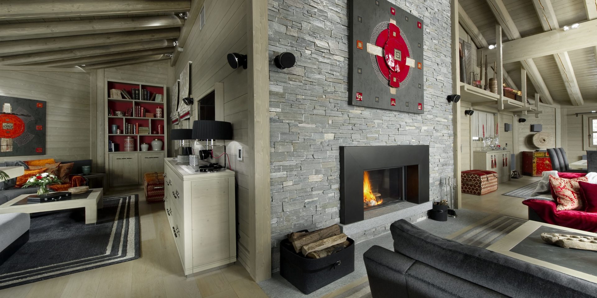 Le K2 Palace Suite-Chalet Baltoro Courchevel Les 3 Vallees Frankrijk wintersport skivakantie luxe living open haard kunst hout banken rode kussens kleed vloerkleed rode kist salontafels stenen muur houten balken