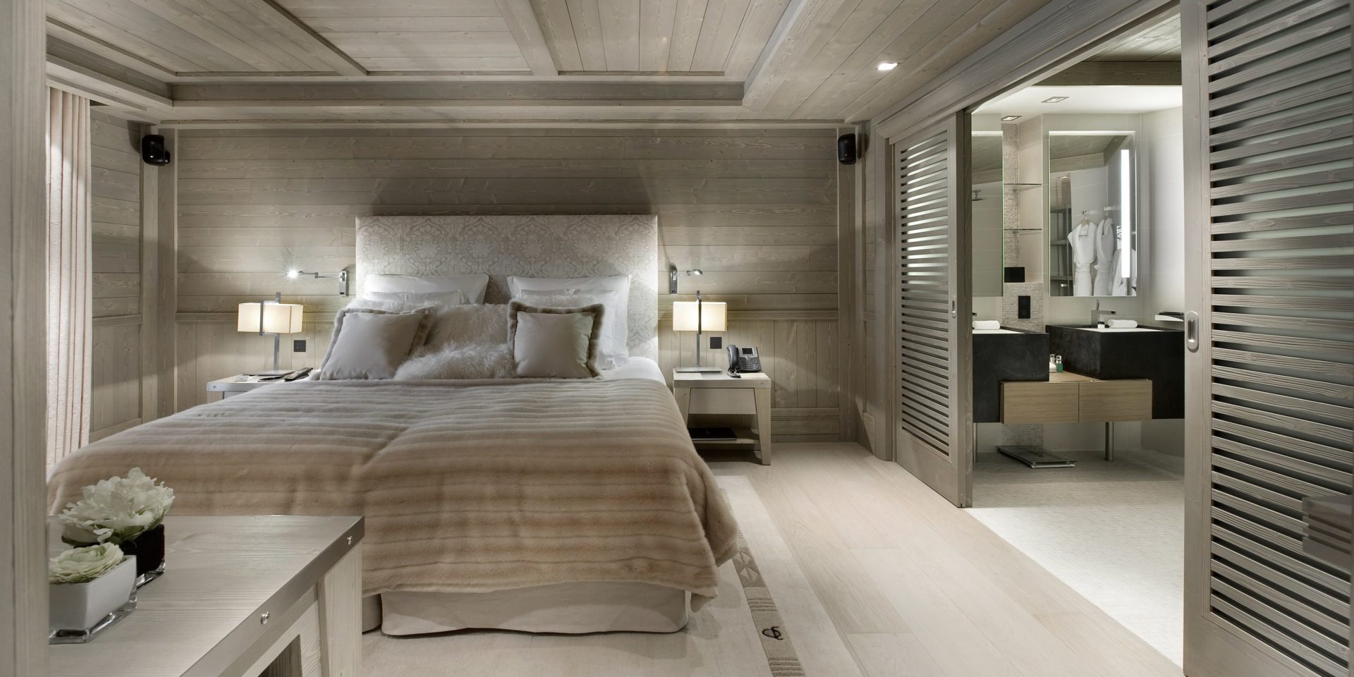 Le K2 Palace Suite-Chalet Karakoram Courchevel Les 3 Vallees Frankrijk wintersport skivakantie luxe slaapkamer 2-persoonsbed hoofdbord kussens kastje houten wanden houten plafond badkamer dubbele wastafel spiegels badjassen