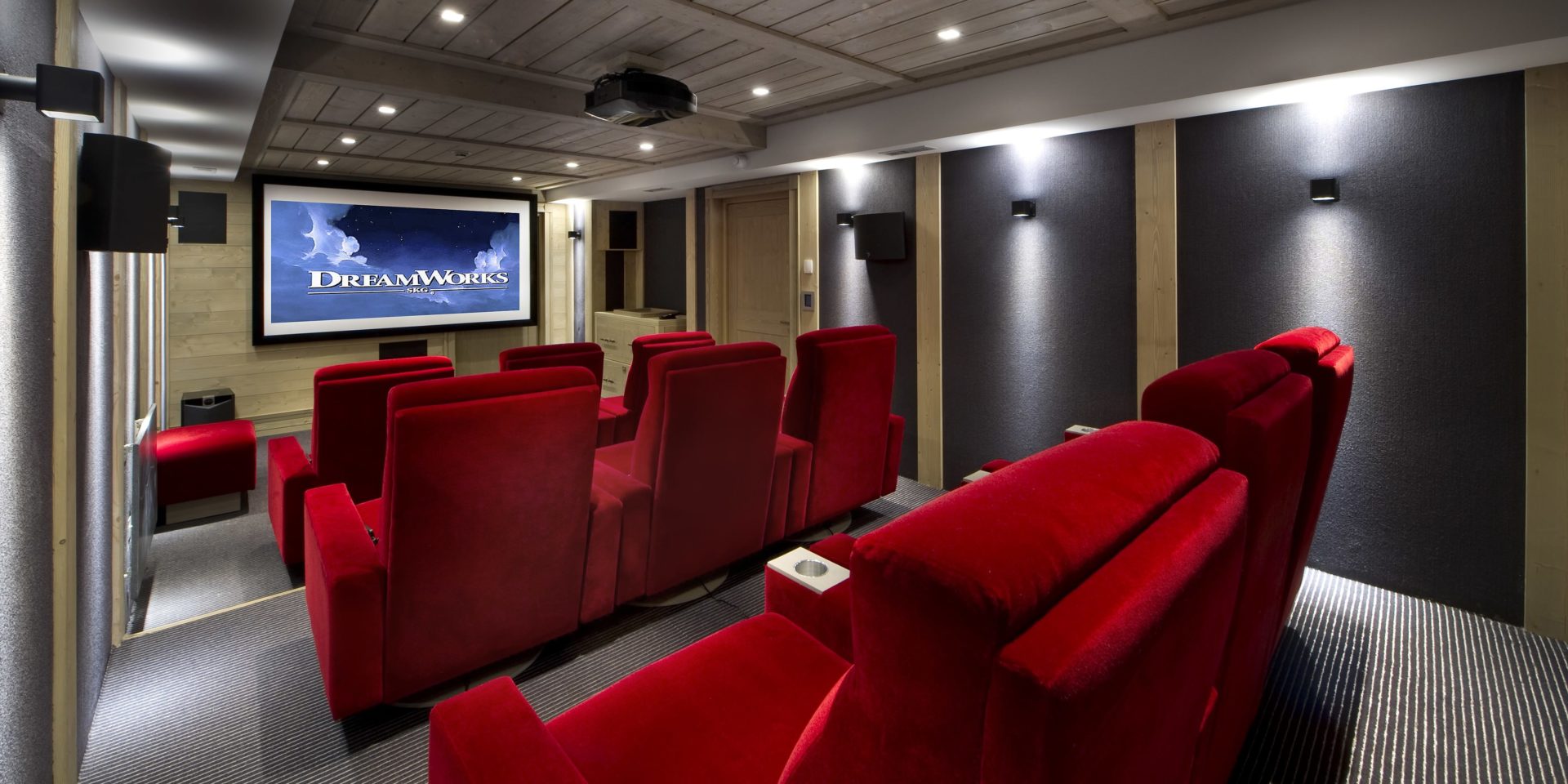 Le K2 Palace Suite-Chalet Muztagh Courchevel Les 3 Vallees Frankrijk wintersport skivakantie luxe bioscoop rode fauteuils rode hocker wandverlichting grote flatscreen houten plafond