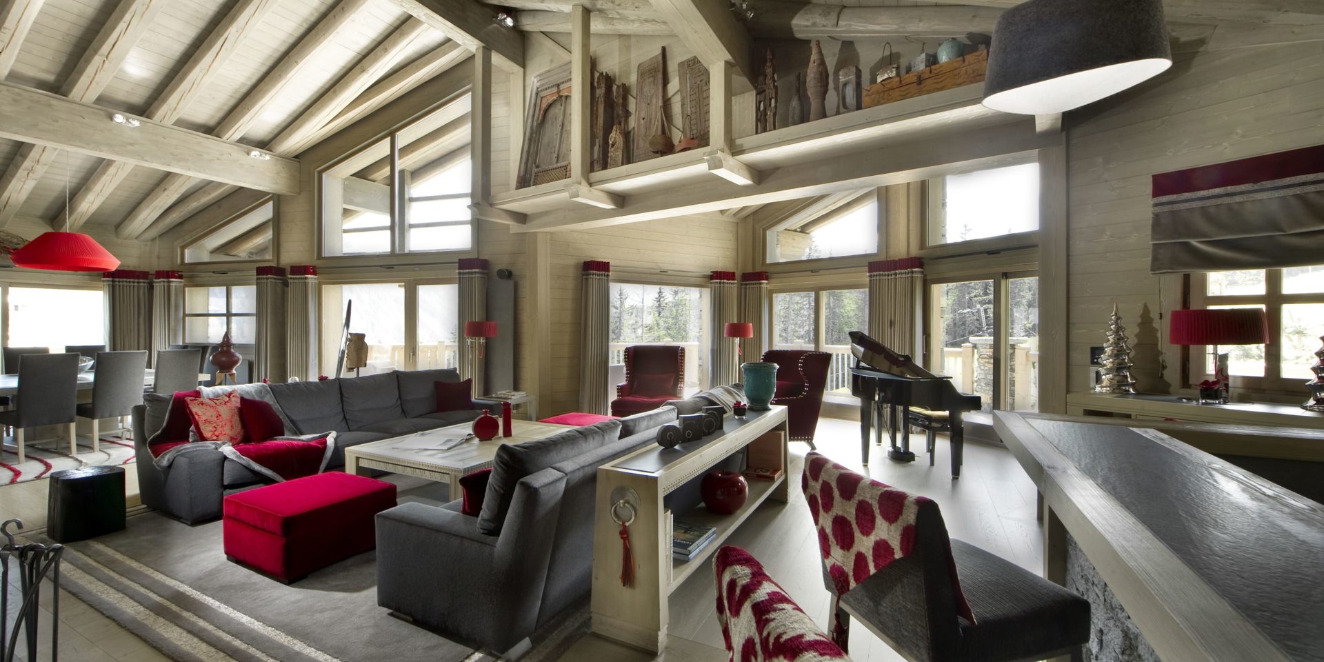 Le K2 Palace Suite-Chalet Muztagh Courchevel Les 3 Vallees Frankrijk wintersport skivakantie luxe living grote grijze banken rode kussens vloerkleed rode hocker eetkamer rode hanglamp bar barkrukken ramen dennenboom houten balken bomen
