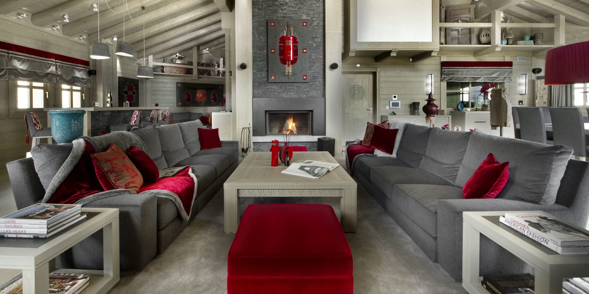 Le K2 Palace Suite-Chalet Muztagh Courchevel Les 3 Vallees Frankrijk wintersport skivakantie luxe living open haard grote grijze banken rode kussens rood kleed rode hocker salontafels kunst houten balken