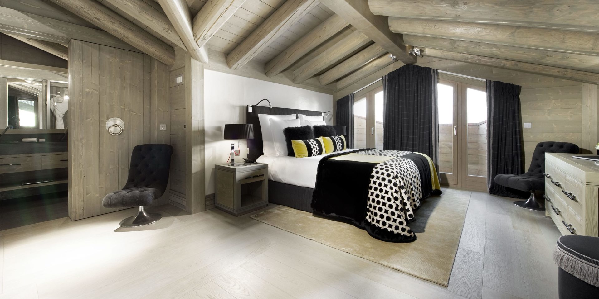 Le K2 Palace Suite-Chalet Muztagh Courchevel Les 3 Vallees Frankrijk wintersport skivakantie luxe slaapkamer 2-persoonsbed geel zwarte kussens geblokte sprei zwarte fauteuils dressoir vloerkleed badkamer spiegel badjas hoge ramen balkon houten balken