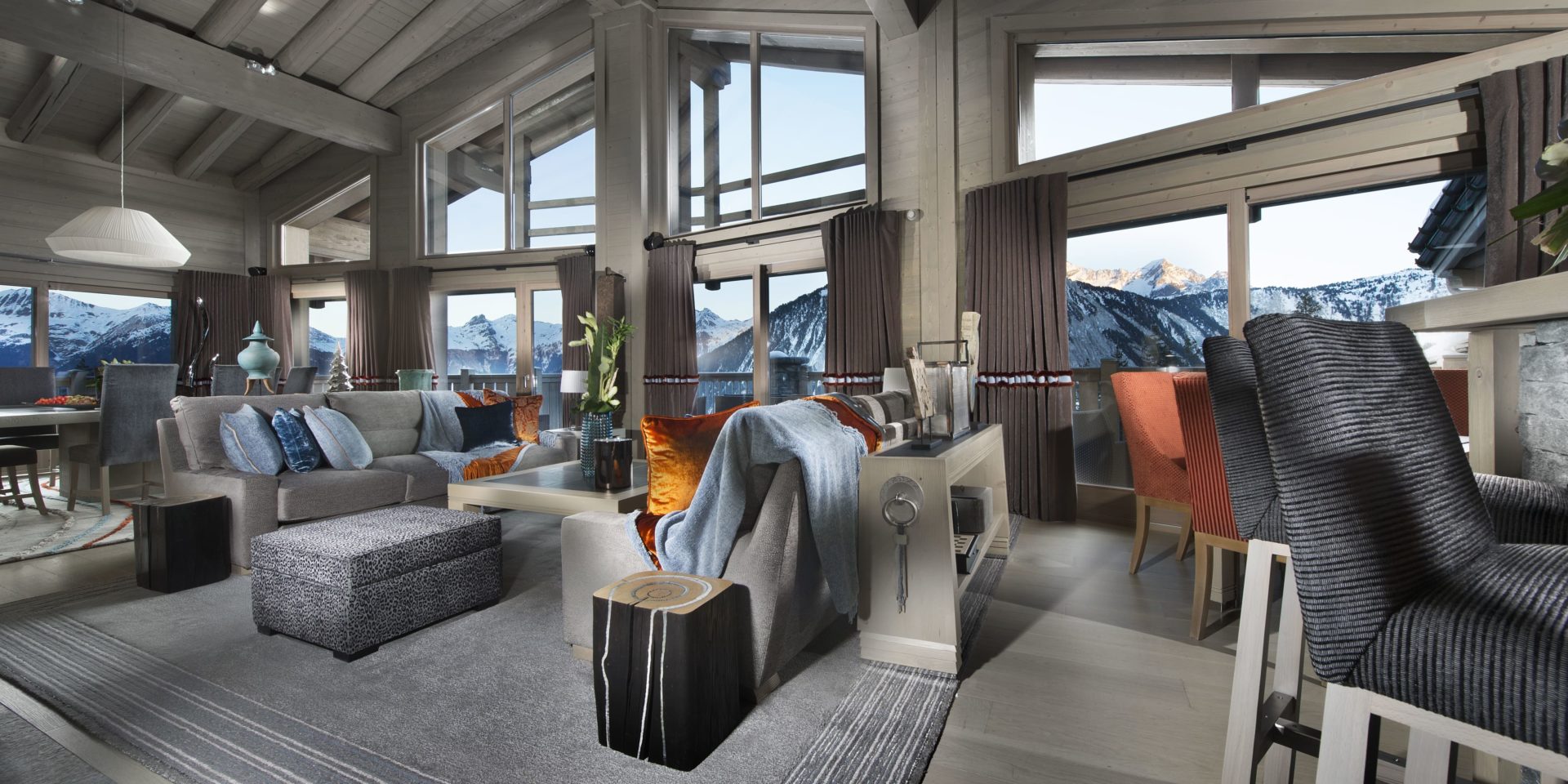 Le K2 Palace Suite-Chalet Panmah Courchevel Les 3 Vallees Frankrijk wintersport skivakantie luxe living bar barkrukken grijze banken oranje kussens salontafel hocker vloerkleed oranje stoelen eetkamer hanglamp hoge ramen houten balken besneeuwde bergen sneeuw