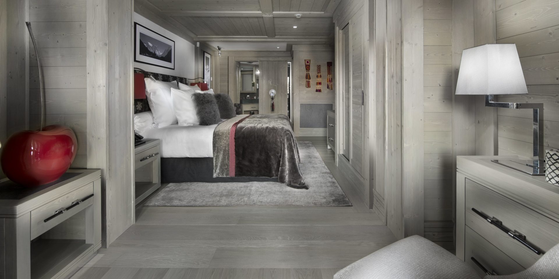 Le K2 Palace Suite-Chalet Panmah Courchevel Les 3 Vallees Frankrijk wintersport skivakantie luxe slaapkamer 2-persoonsbed sprei kussens vloerkleed rode appel fauteuil schilderij badkamer houten wanden houten plafond