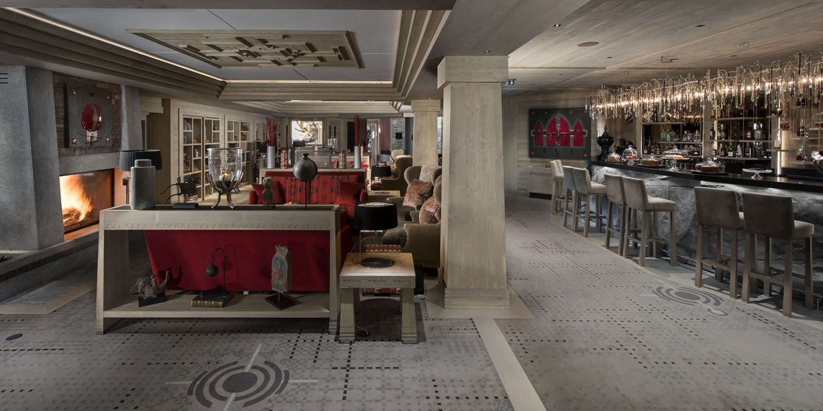 Hotel Le K2 Altitude Courchevel Les 3 Vallees Frankrijk wintersport skivakantie luxe lounge rode banken fauteuils open haard bar barkrukken verlichting vloerbedekking houten pilaren
