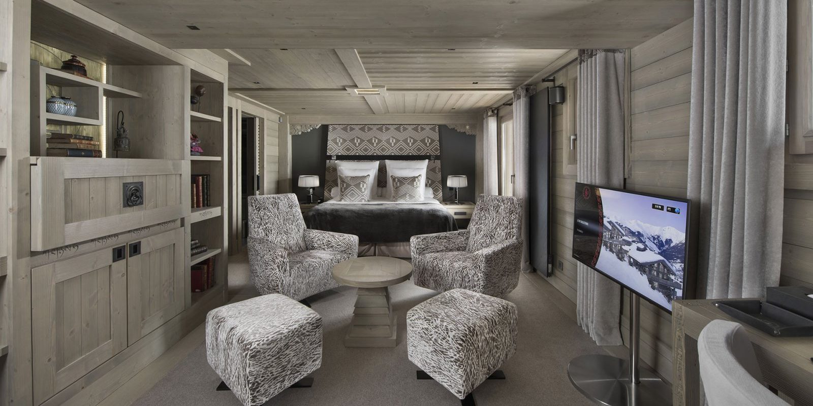 Hotel Le K2 Altitude Courchevel Les 3 Vallees Frankrijk wintersport skivakantie luxe slaapkamer 2-persoonsbed wit bruine fauteuils hockers salontafel TV houten wandkast houten plafonds
