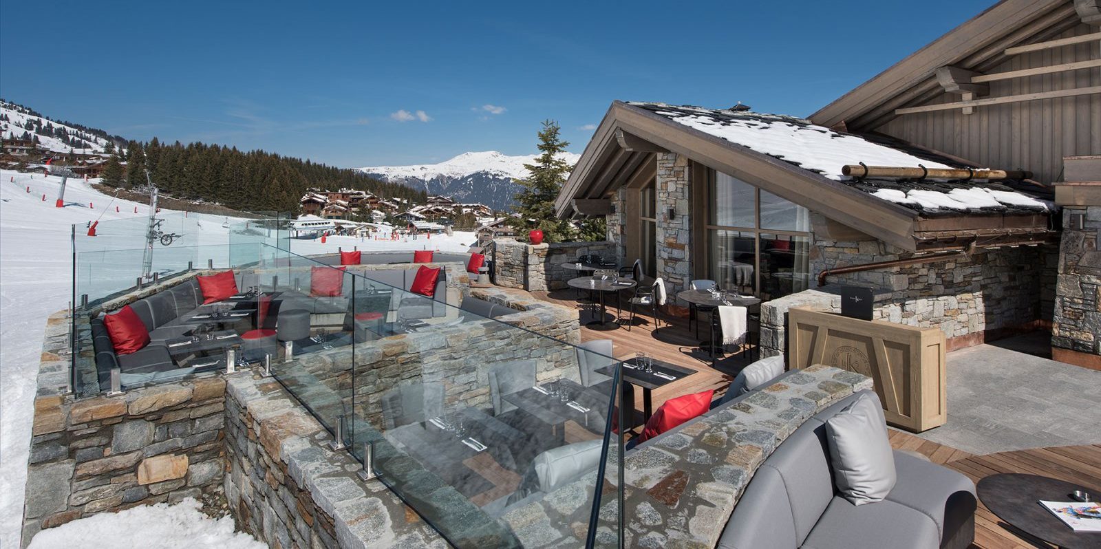 Hotel Le K2 Altitude Courchevel Les 3 Vallees Frankrijk wintersport skivakantie luxe groot terras banken rode kussens houten vlonder piste bomen bergen sneeuw