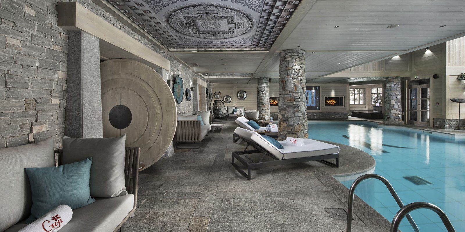 Hotel Le K2 Altitude Courchevel Les 3 Vallees Frankrijk wintersport skivakantie luxe zwembad banken loungestoelen blauwe kussens hangende stoel stenen pilaren ronde deur houten plafond open haard zwemmen ontspannen relaxen genieten