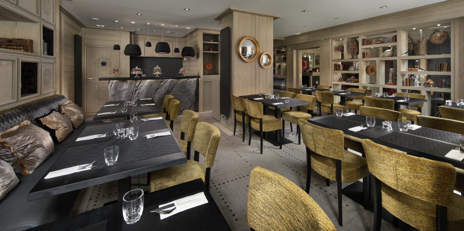 Hotel Le K2 Djola Courchevel Les 3 Vallees Frankrijk wintersport skivakantie luxe eetkamer zwarte leren bank bruine kussens groene stoffen stoelen houten wandkast bar hanglampen spiegels hout