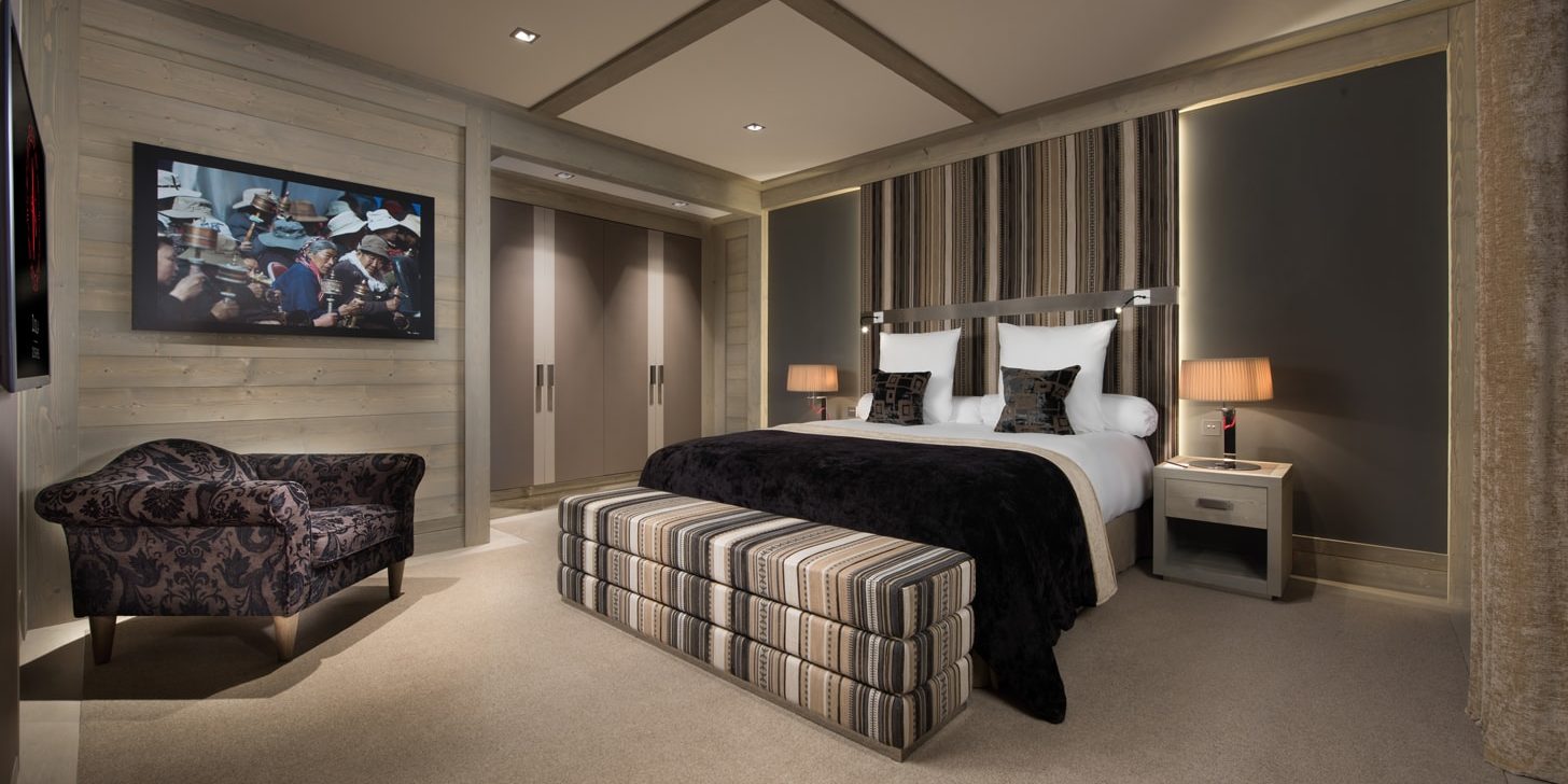 Hotel Le K2 Djola Courchevel Les 3 Vallees Frankrijk wintersport skivakantie luxe slaapkamer 2-persoonsbed hocker TV fauteuil schilderij hout gestreept behang vloerbedekking