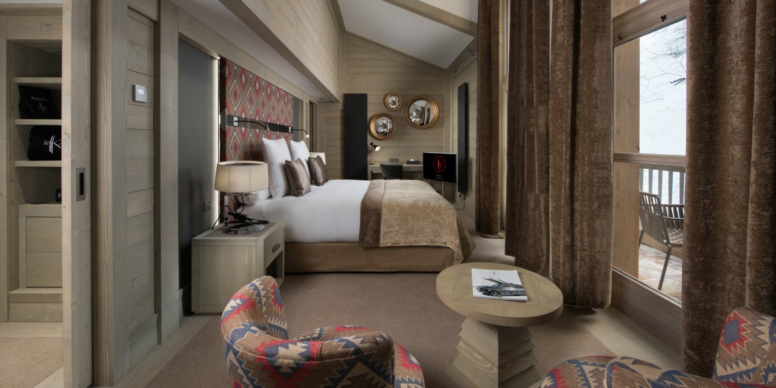 Hotel Le K2 Djola Courchevel Les 3 Vallees Frankrijk wintersport skivakantie luxe slaapkamer 2-persoonsbed TV fauteuils salontafel spiegels hout hoge ramen balkon uitzicht bomen sneeuw