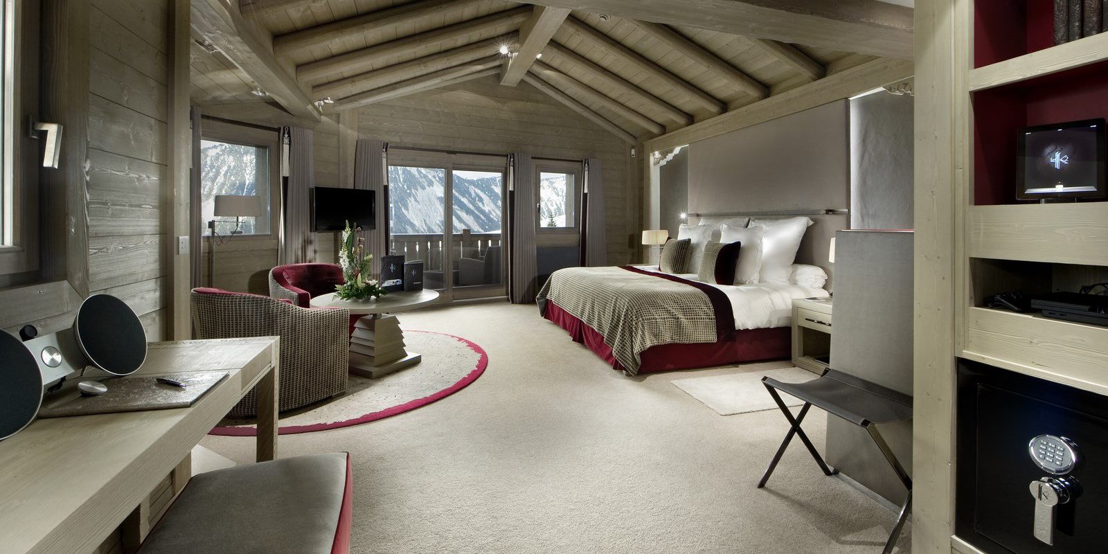 Hotel Le K2 Palace Courchevel Les 3 Vallees Frankrijk wintersport skivakantie luxe slaapkamer 2-persoonsbed rood bruine fauteuils salontafel bureau hocker kussens houten balken houten plafond balkon besneeuwde bergen sneeuw